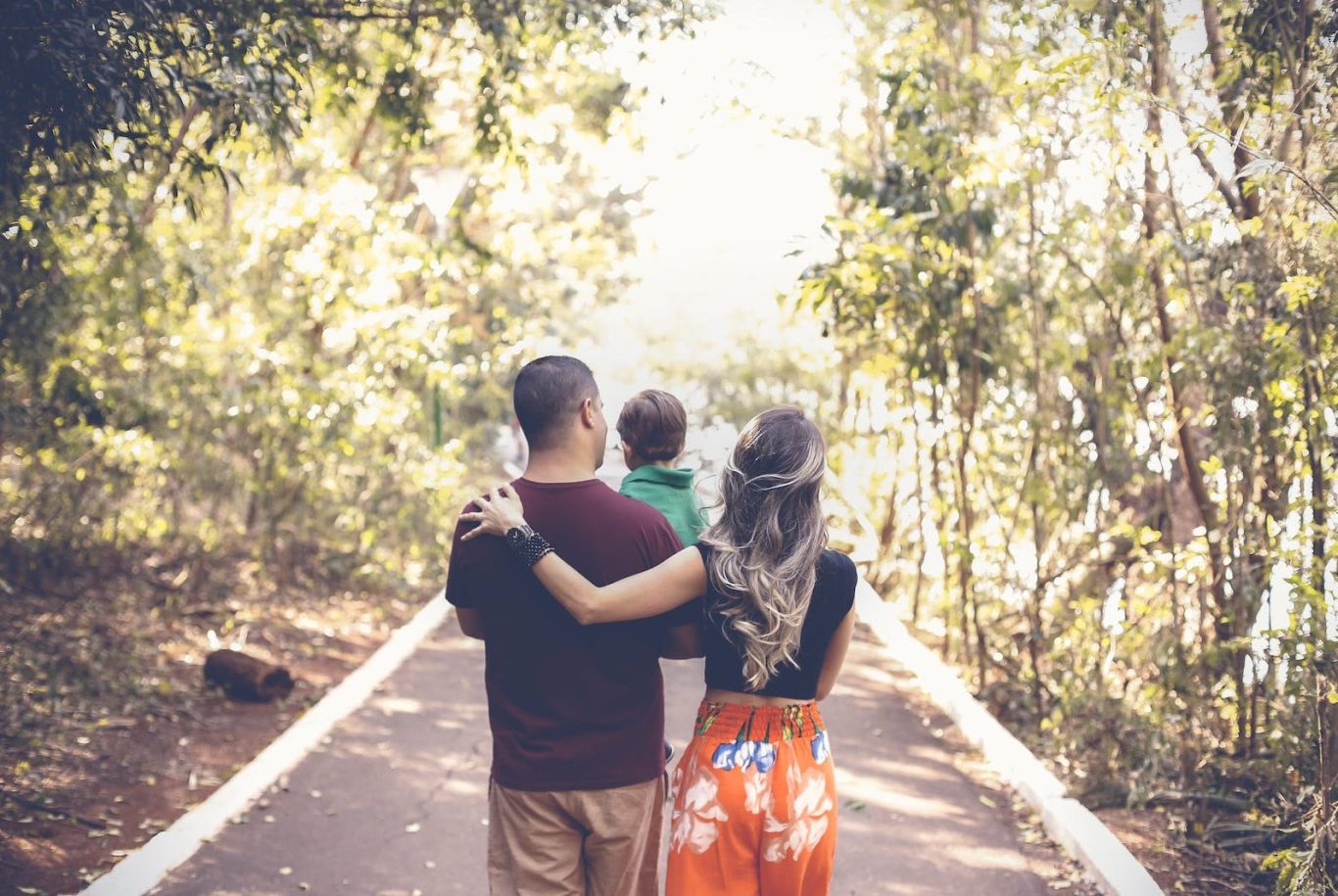 Un papa et une maman se promène avec leur enfant. Le papa tiens l'enfant dans ses bras 